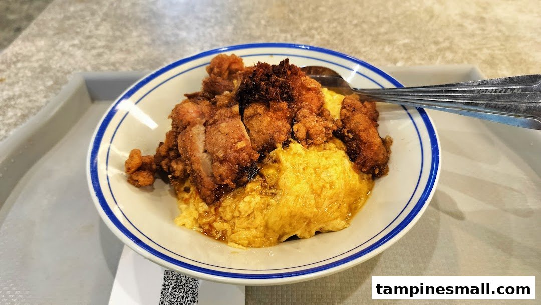 A delicious bowl of scrambled egg rice topped with crispy fried chicken, served on a tray.