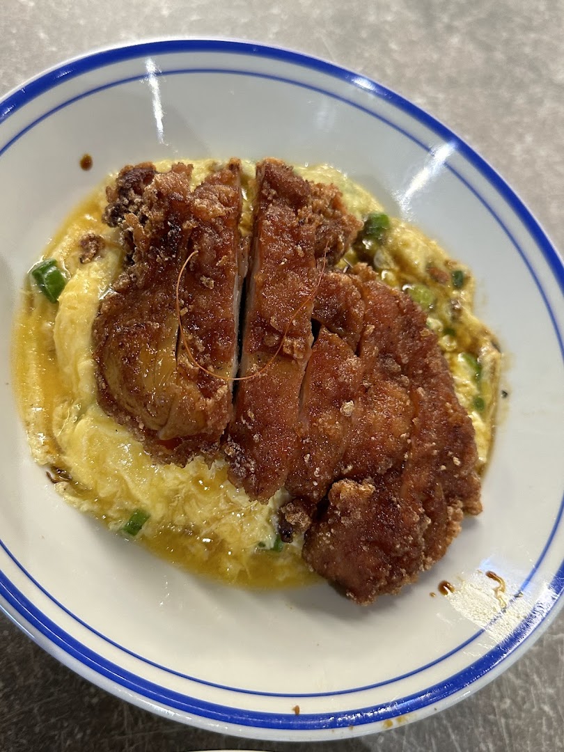 A close-up of crispy fried chicken cutlet served over fluffy scrambled egg rice in a bowl.