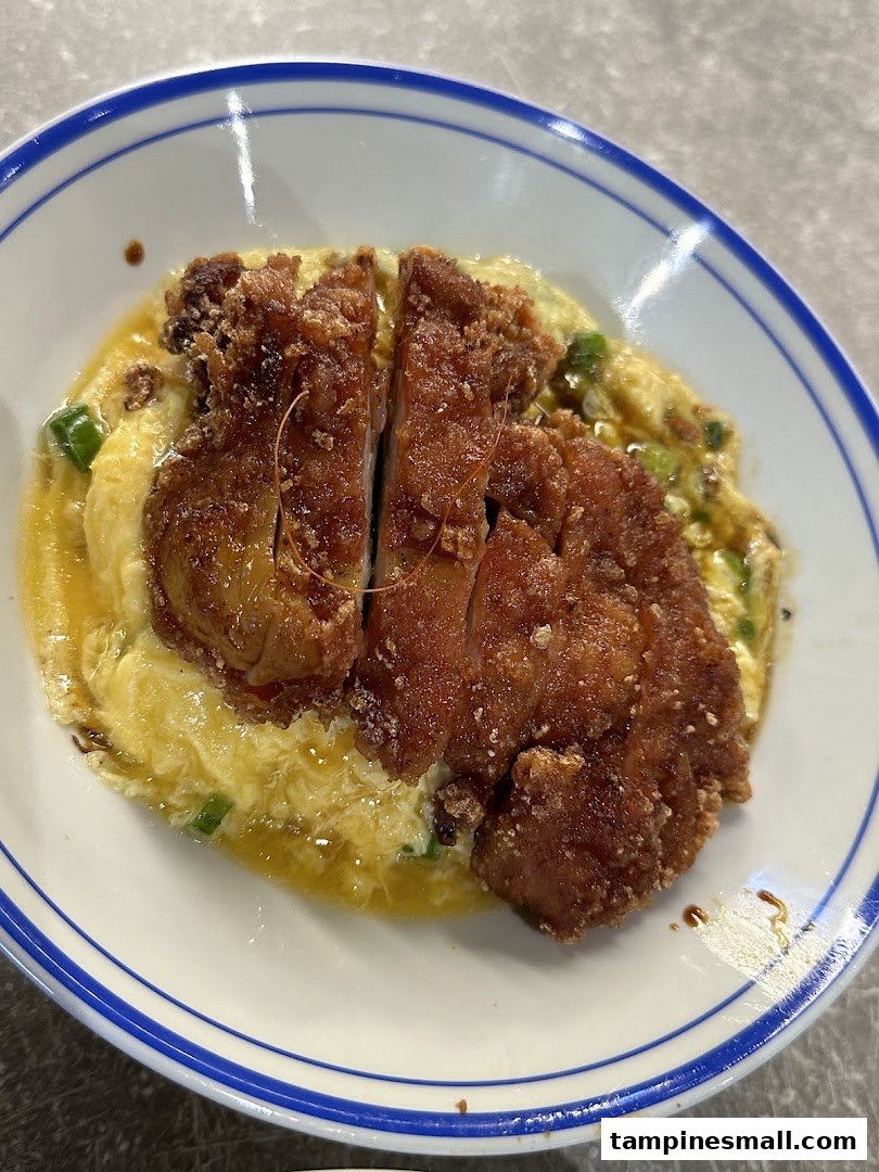 A close-up of crispy fried chicken cutlet served over fluffy scrambled egg rice in a bowl.