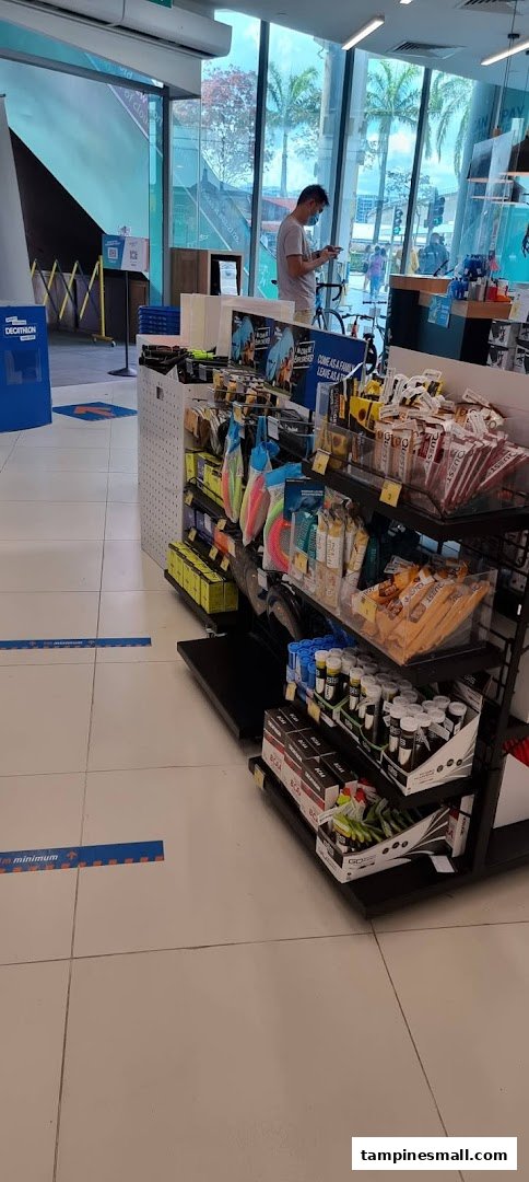 Interior view of Decathlon showing sports nutrition products, accessories, and a customer browsing.