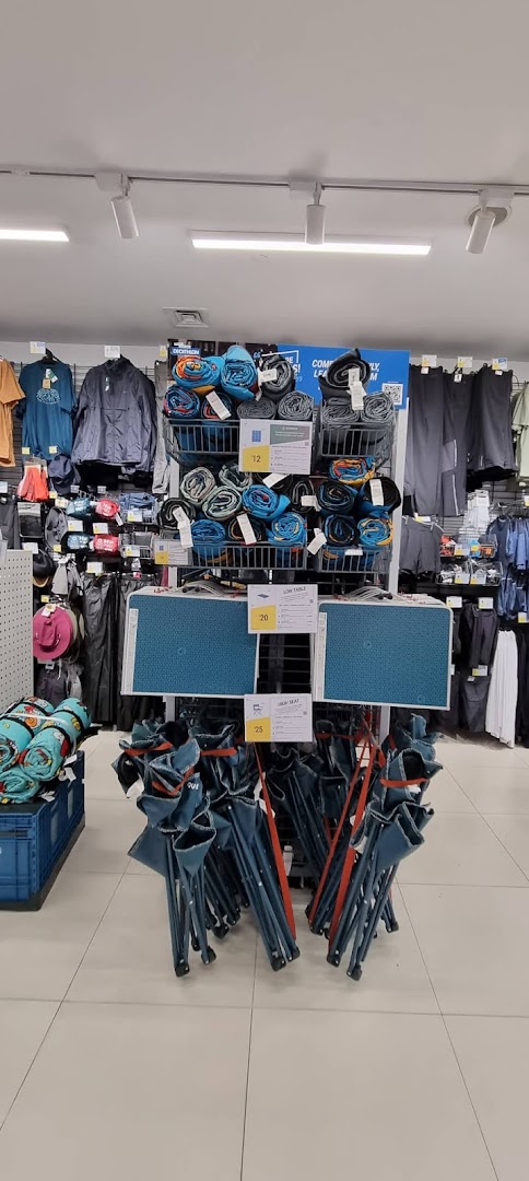 An aisle in Decathlon showcasing camping gear, including rolled mats, folding tables, and chairs.