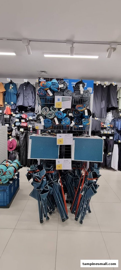 An aisle in Decathlon showcasing camping gear, including rolled mats, folding tables, and chairs.