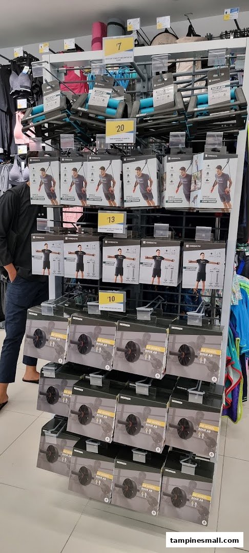 A display of fitness equipment, including ab wheels, suspension trainers, and push-up bars, inside a Decathlon store.