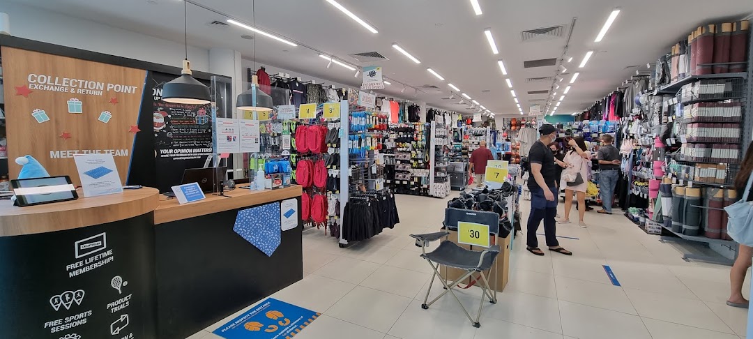 Interior view of Decathlon, showcasing sports equipment, apparel, and a collection point with customers browsing.