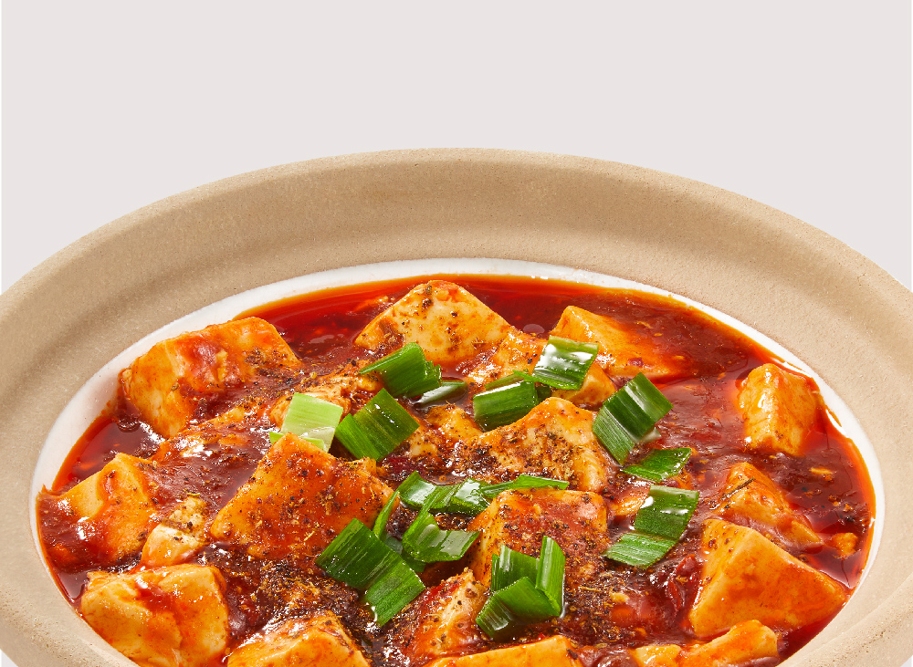 A close-up of a spicy tofu dish with red sauce and green onions in a bowl.