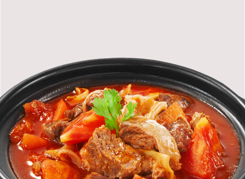 A close-up of a hearty beef stew with tomatoes and other ingredients in a black bowl.