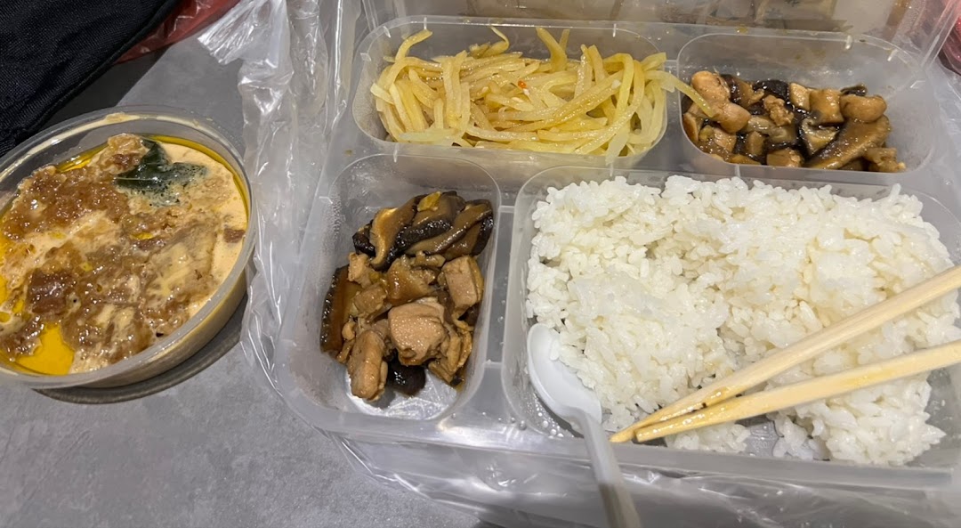 A bento box with rice, various side dishes, and a separate bowl of curry or stew.