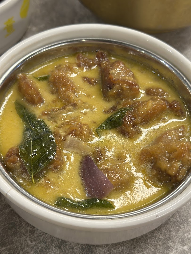 A close-up of a delicious-looking curry dish with meat pieces and herbs in a white bowl.