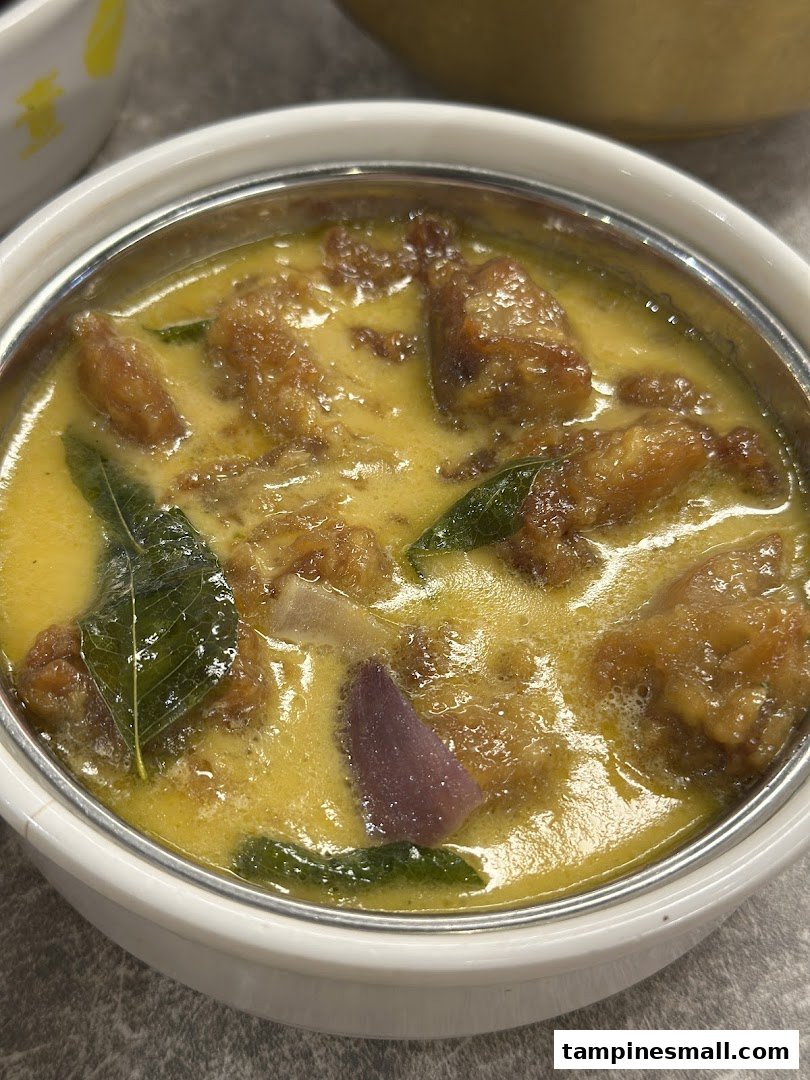 A close-up of a delicious-looking curry dish with meat pieces and herbs in a white bowl.