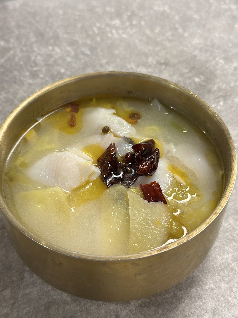 A close-up of a bowl of fish soup with vegetables and chili in a brass bowl.
