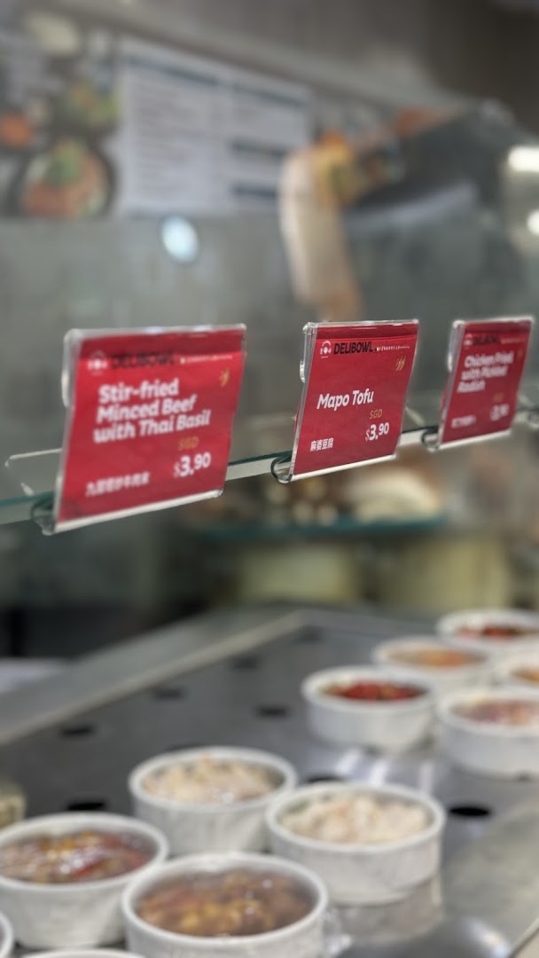 Close-up of prepared food items in a display case with price tags at Delibowl Rice Kitchen.