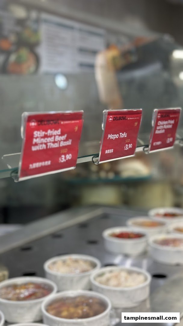 Close-up of prepared food items in a display case with price tags at Delibowl Rice Kitchen.
