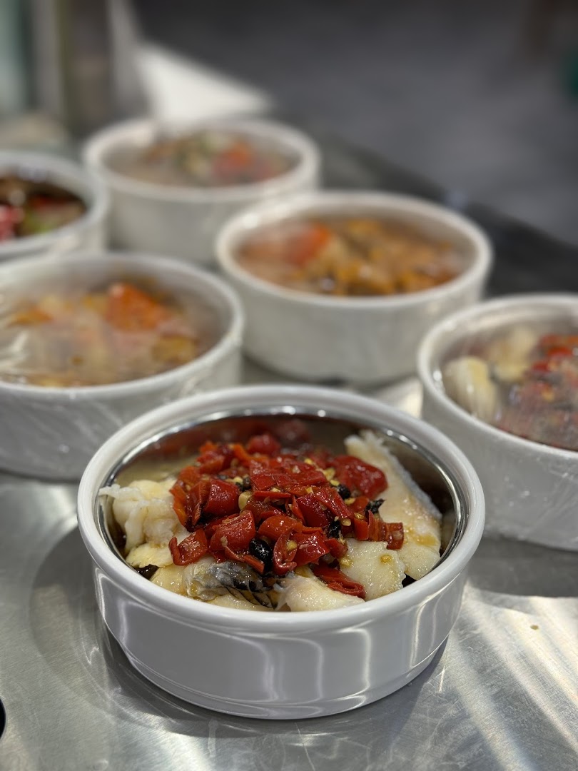 Close-up of several bowls of freshly prepared food, featuring a dish with fish and red peppers.