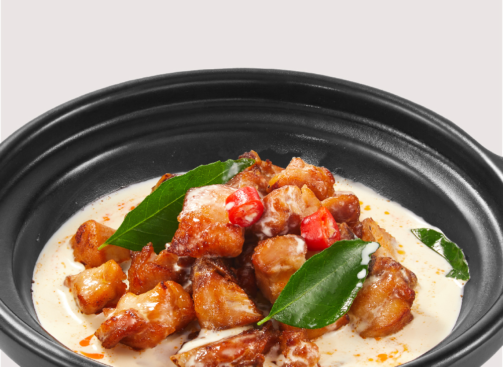 Golden-brown chicken pieces in creamy sauce with chilies and curry leaves in a black bowl.