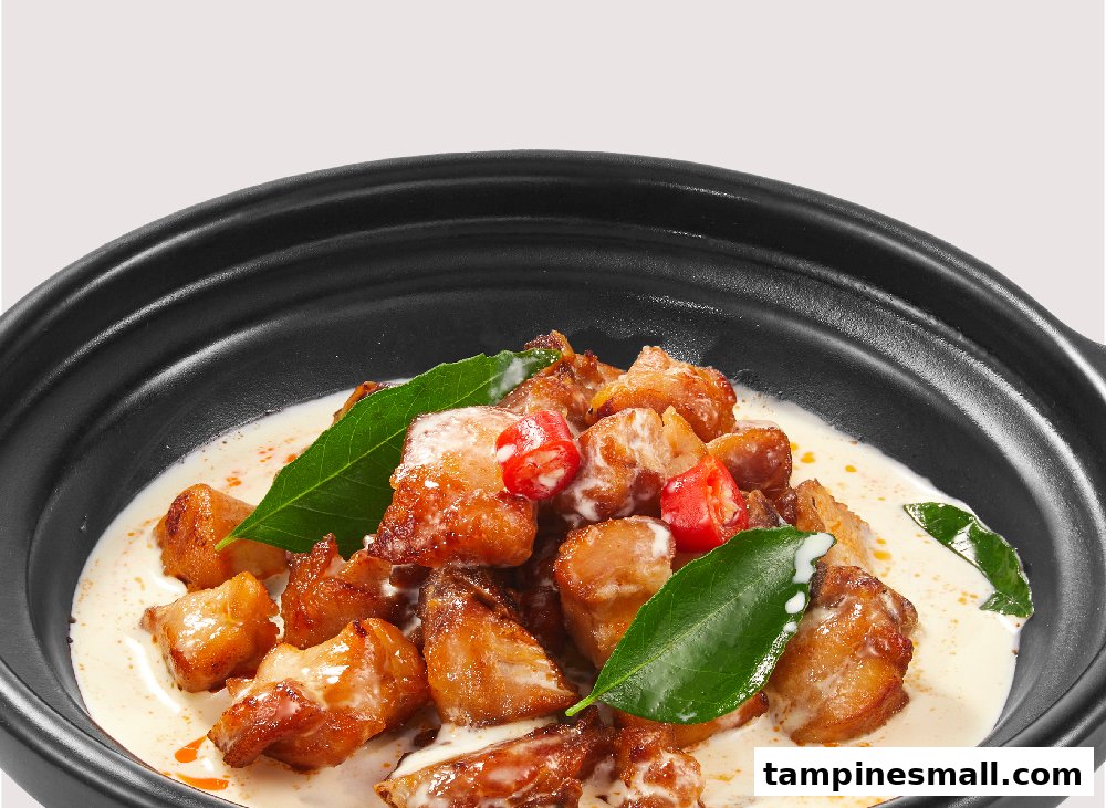 Golden-brown chicken pieces in creamy sauce with chilies and curry leaves in a black bowl.
