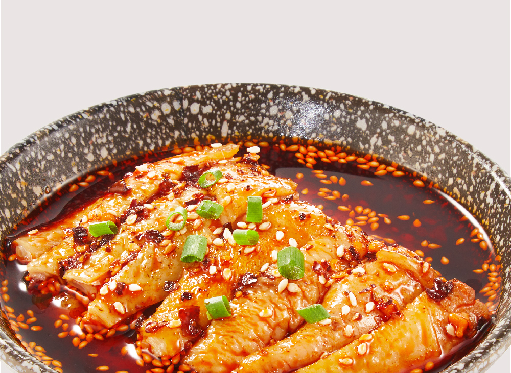 Close-up of spicy chicken in a dark sauce, garnished with sesame seeds and spring onions.