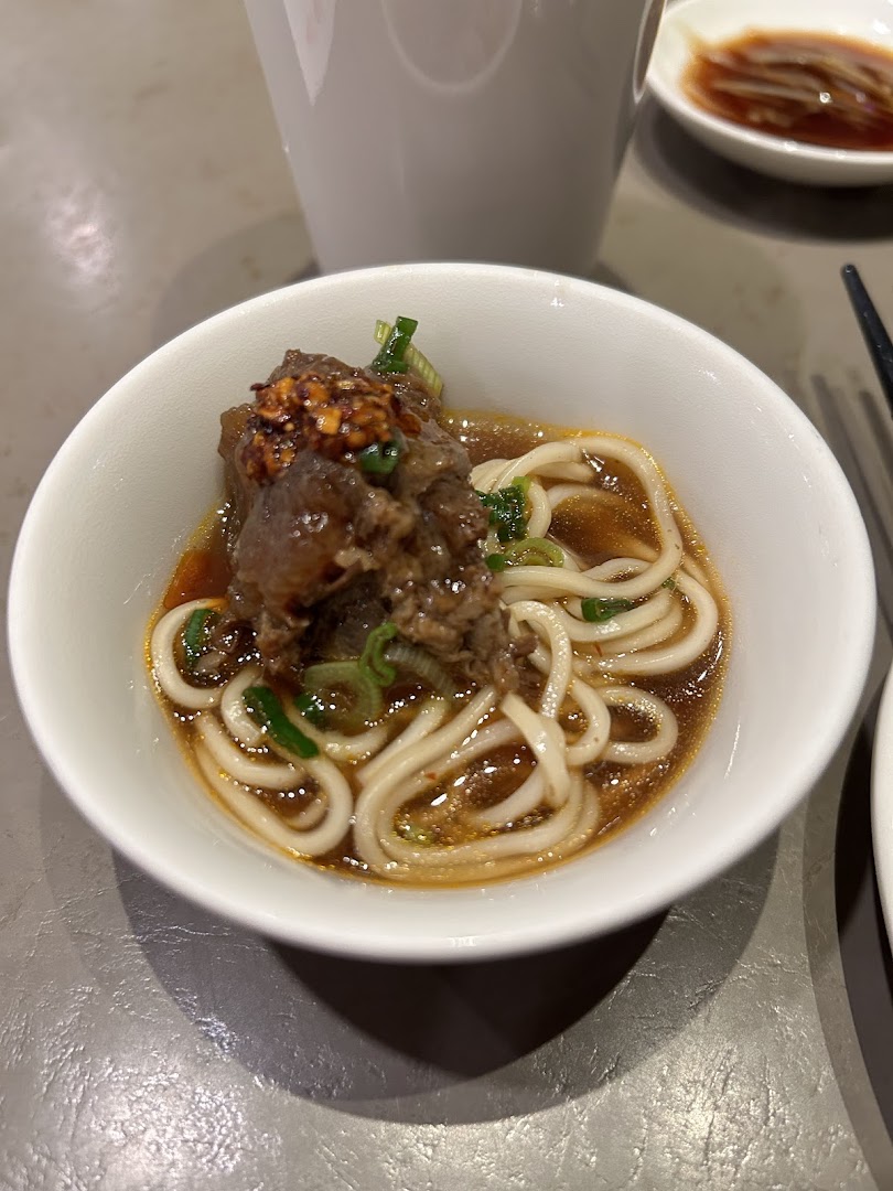 A close-up of a bowl of Din Tai Fung's signature beef noodles with rich broth and tender meat.