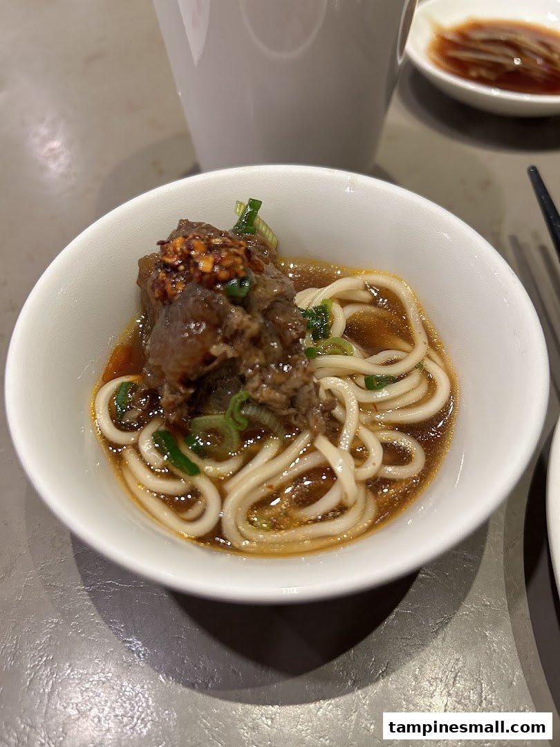 A close-up of a bowl of Din Tai Fung's signature beef noodles with rich broth and tender meat.