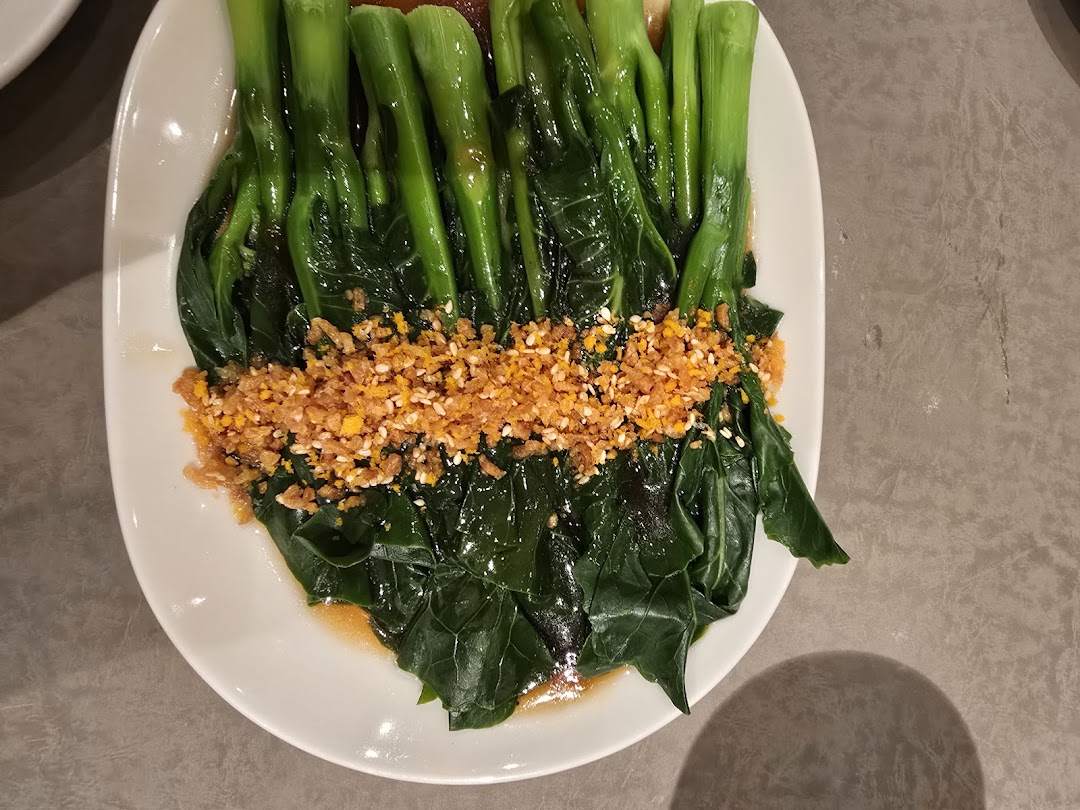 A plate of vibrant green vegetables topped with crispy garlic and sesame seeds, served at Din Tai Fung.