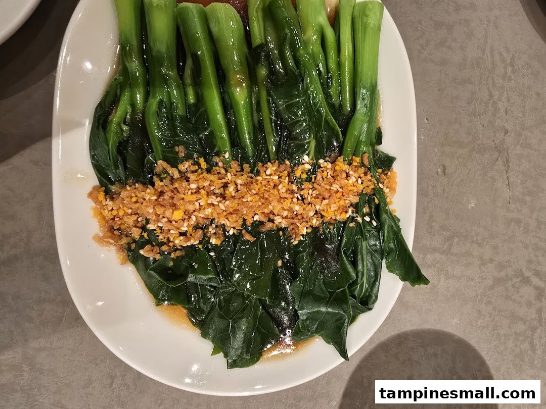 A plate of vibrant green vegetables topped with crispy garlic and sesame seeds, served at Din Tai Fung.