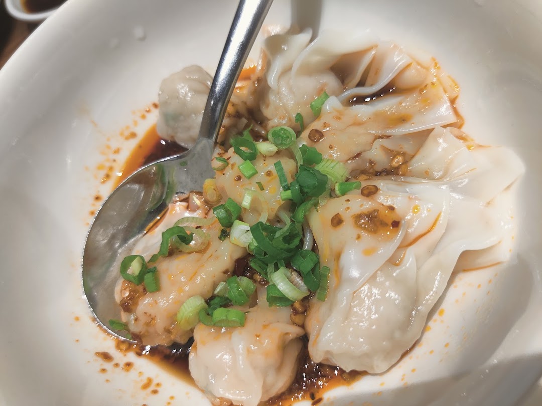 A close-up of delicious Din Tai Fung dumplings or wontons in chili oil, garnished with green onions.