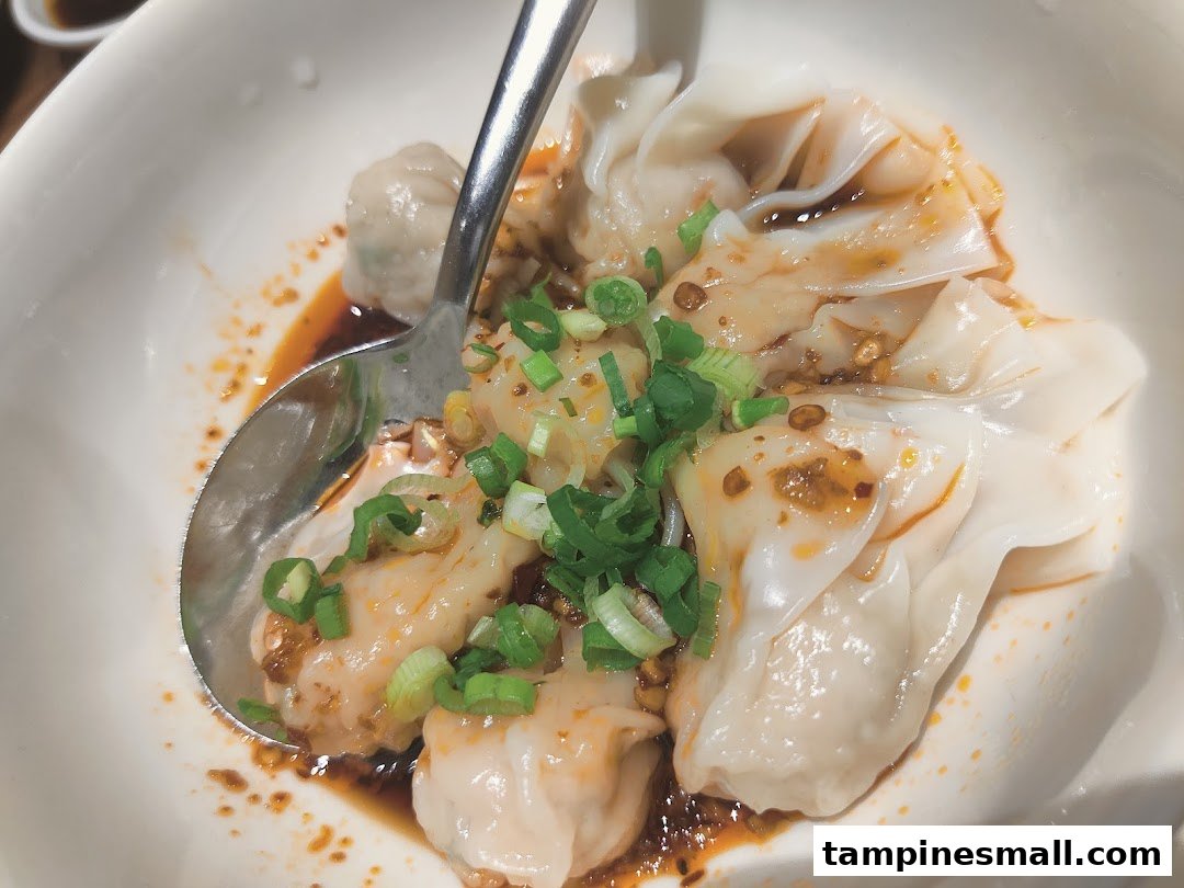 A close-up of delicious Din Tai Fung dumplings or wontons in chili oil, garnished with green onions.