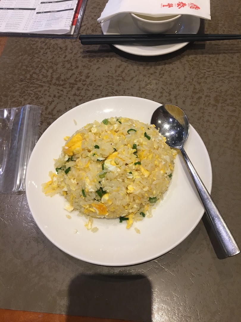A delicious plate of egg fried rice with green onions and a spoon on a white plate.