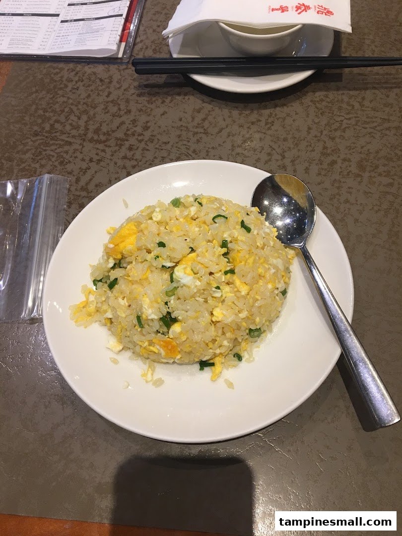 A delicious plate of egg fried rice with green onions and a spoon on a white plate.