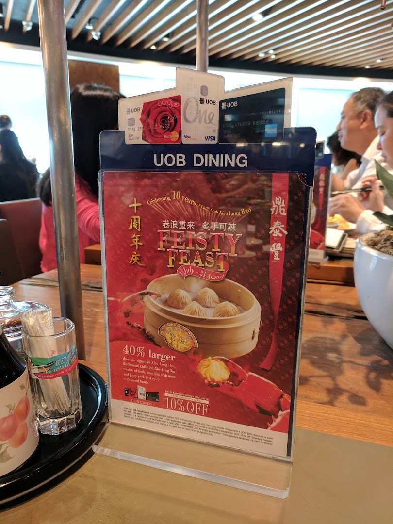A promotional stand for Din Tai Fung's 'Feisty Feast' featuring Chili Crab Xiao Long Bao on a restaurant table.