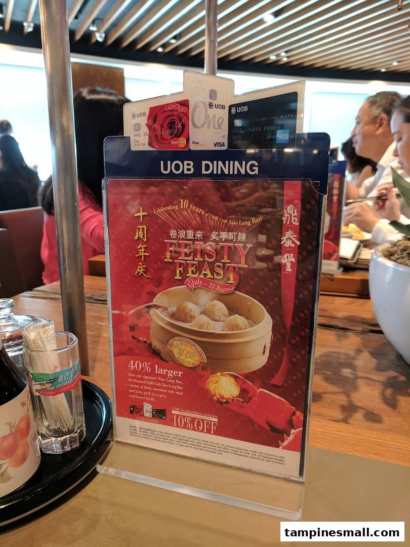 A promotional stand for Din Tai Fung's 'Feisty Feast' featuring Chili Crab Xiao Long Bao on a restaurant table.
