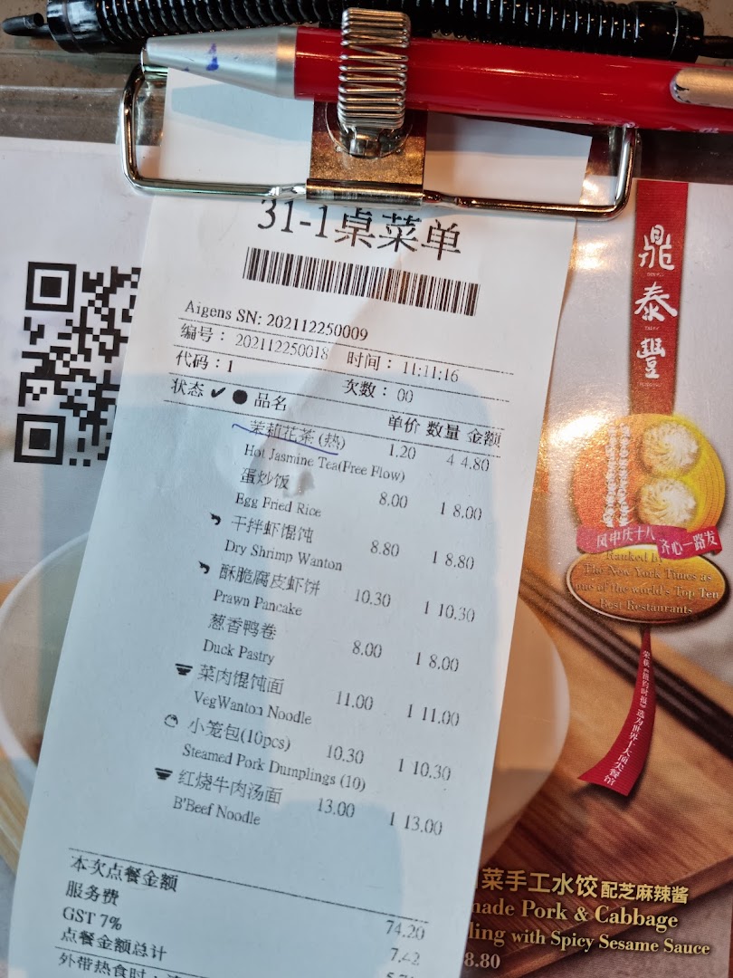 A close-up of a Din Tai Fung order slip/menu with a pen, showing various food items and prices.