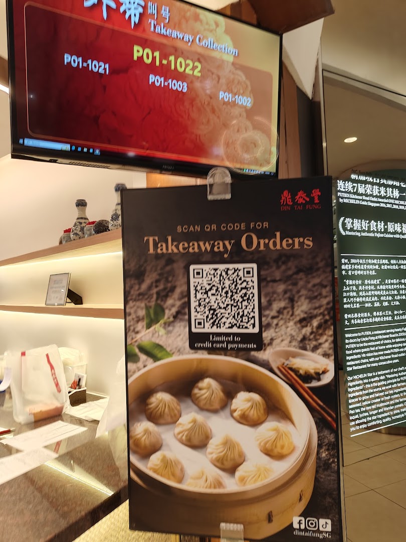 A Din Tai Fung counter displaying takeaway collection numbers and a standee for online orders.