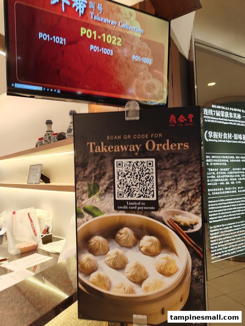 A Din Tai Fung counter displaying takeaway collection numbers and a standee for online orders.