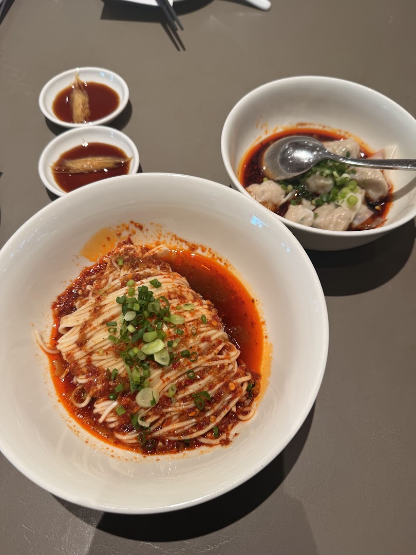 A close-up of spicy noodles and chili oil dumplings served with dipping sauces at Din Tai Fung.