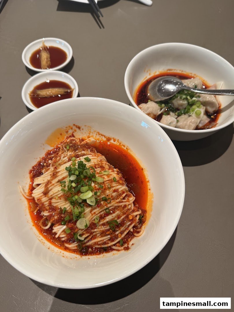 A close-up of spicy noodles and chili oil dumplings served with dipping sauces at Din Tai Fung.