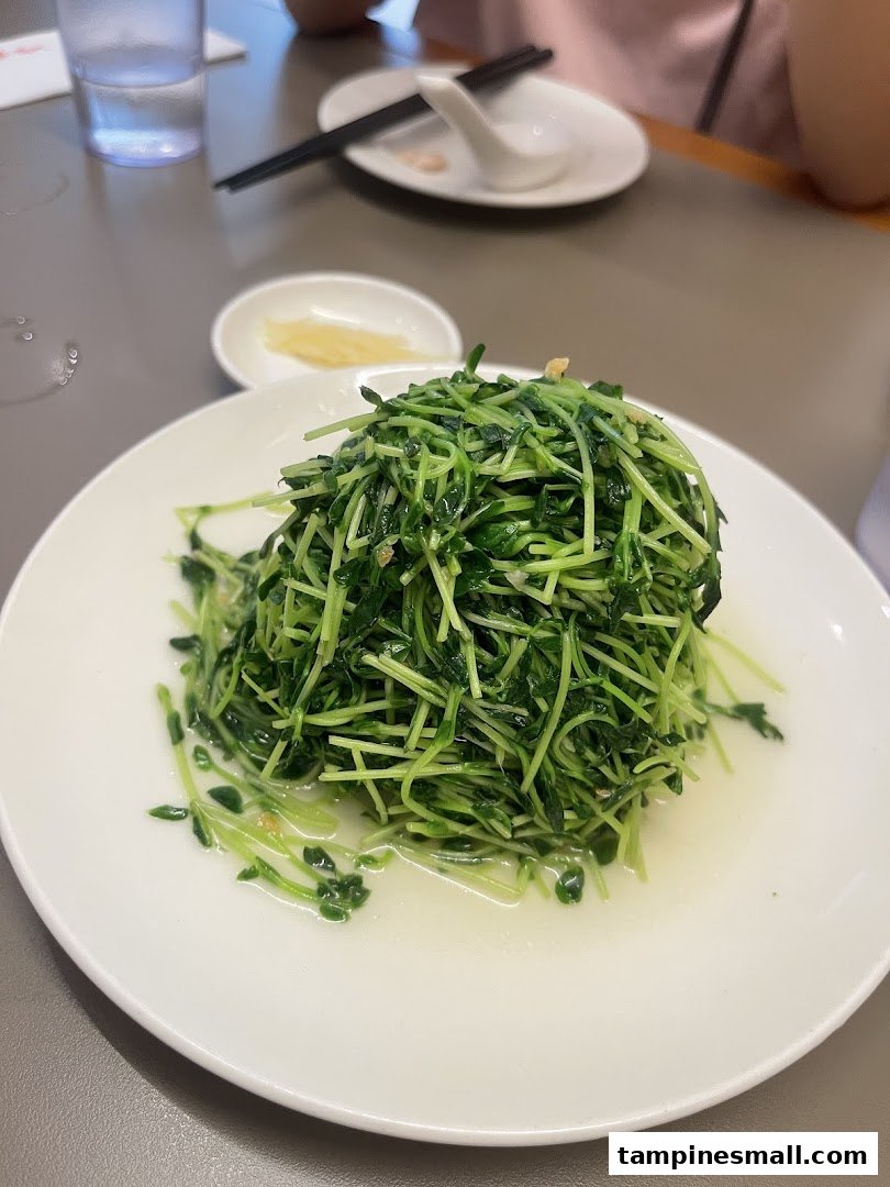 A plate of vibrant green stir-fried pea shoots with a light sauce on a dining table.