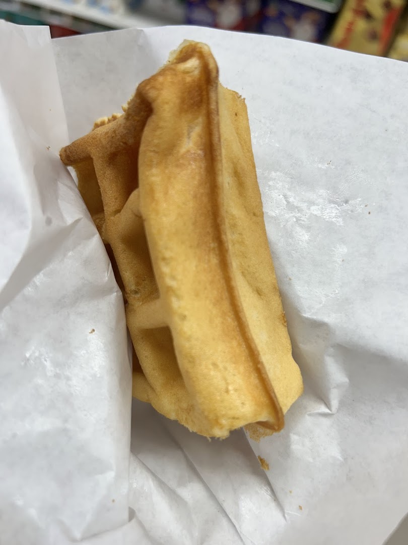 A golden-brown waffle, freshly baked and wrapped in white paper, ready to enjoy.