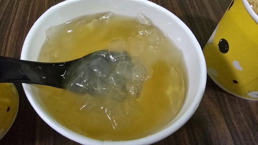 A white bowl filled with a clear, amber-colored jelly dessert and a black spoon.