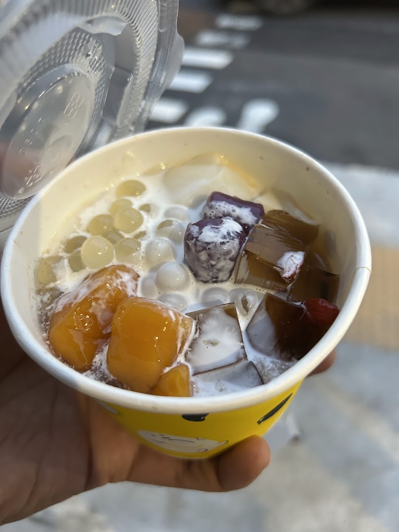 A hand holds a vibrant cup of dessert with various colorful toppings and a clear lid.