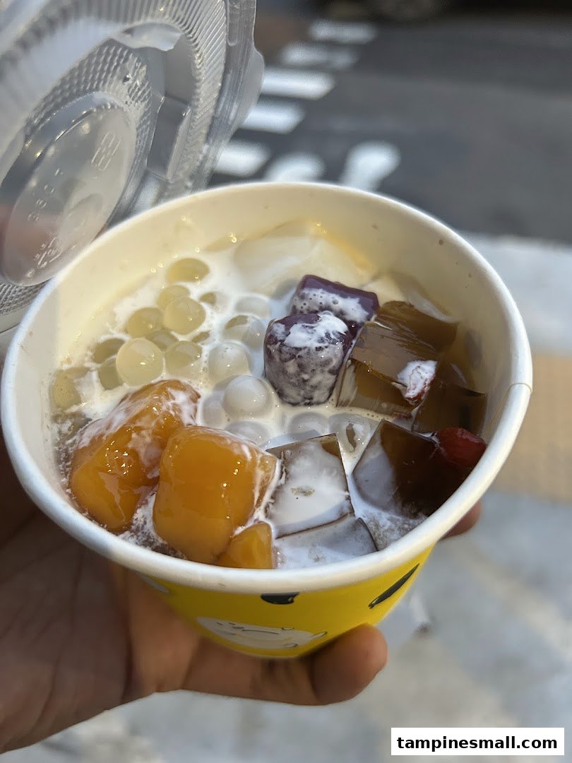 A hand holds a vibrant cup of dessert with various colorful toppings and a clear lid.