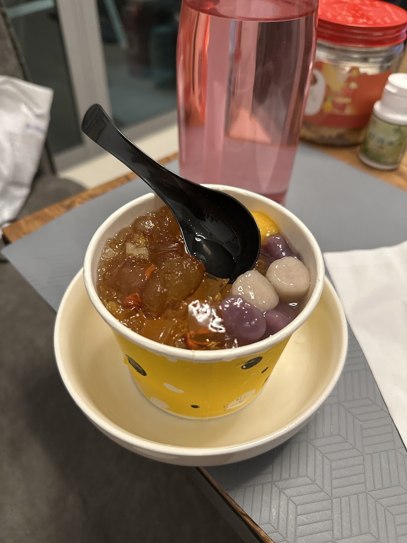 A vibrant cup of traditional Asian dessert with taro balls and sweet toppings, served with a spoon.