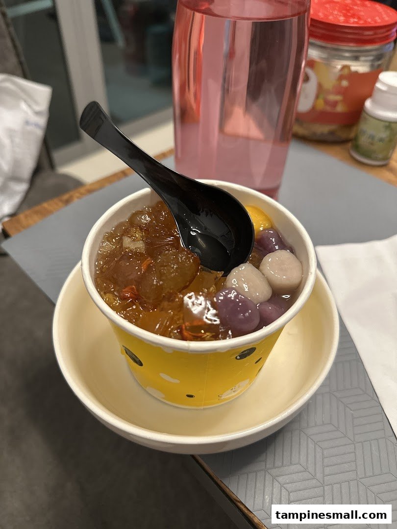 A vibrant cup of traditional Asian dessert with taro balls and sweet toppings, served with a spoon.