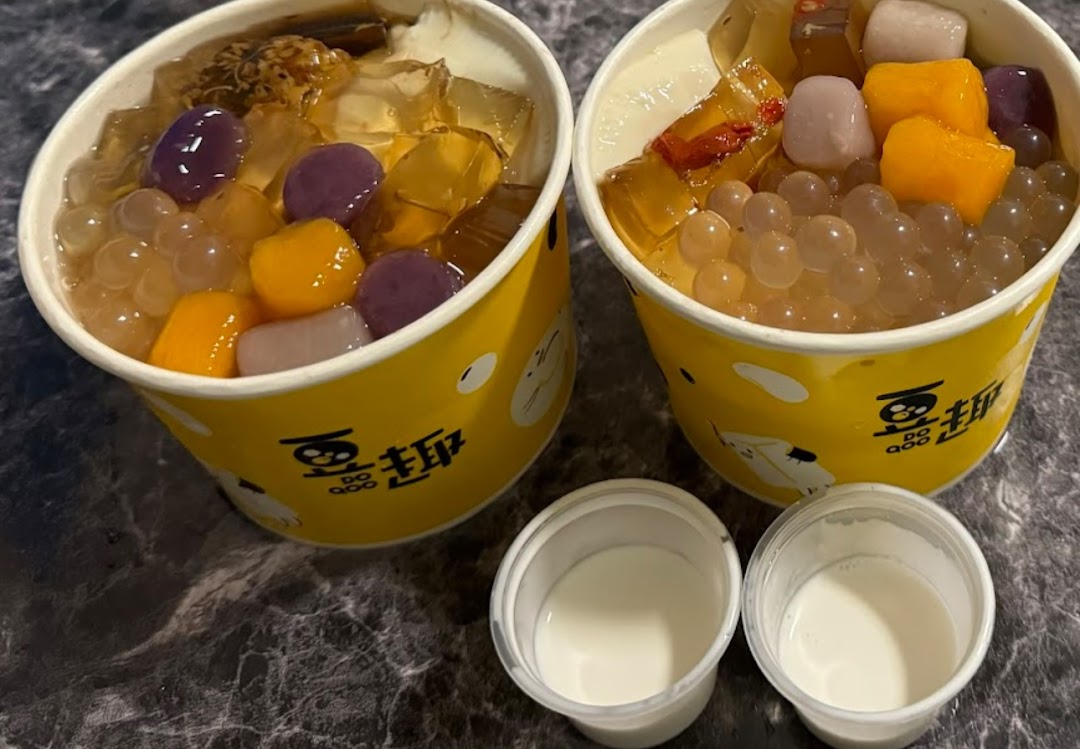 Two vibrant dessert cups from Do Qoo, filled with colorful toppings, jellies, and pearls, alongside two small milk cups.