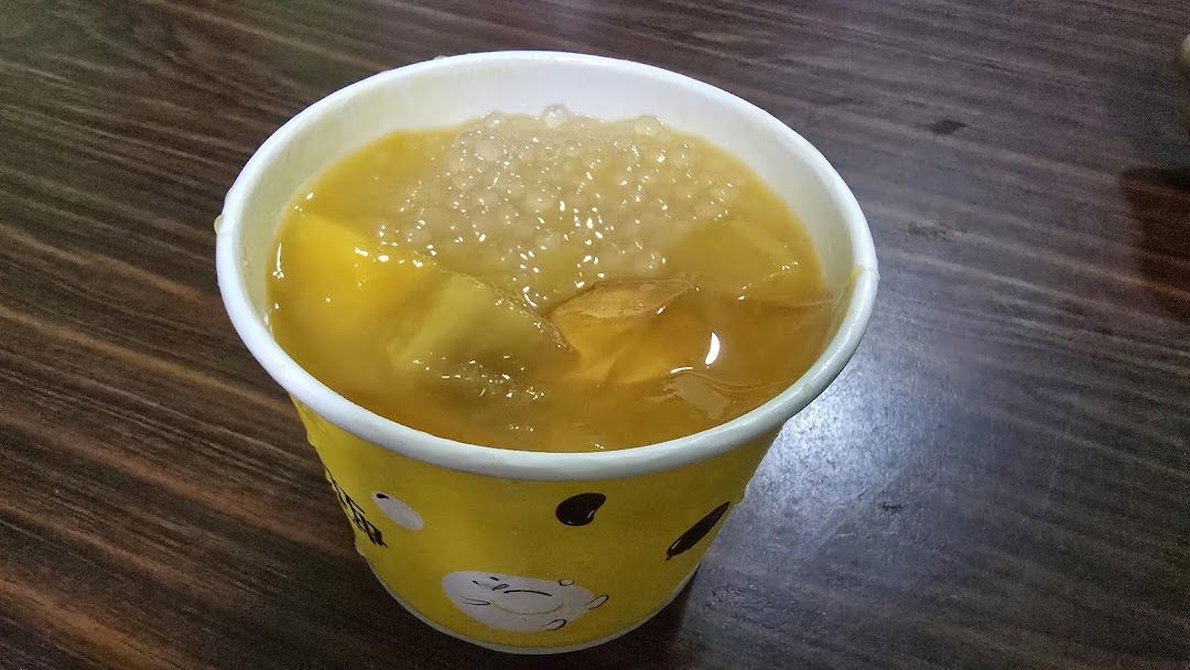A vibrant yellow drink with ice and toppings in a branded cup on a wooden surface.