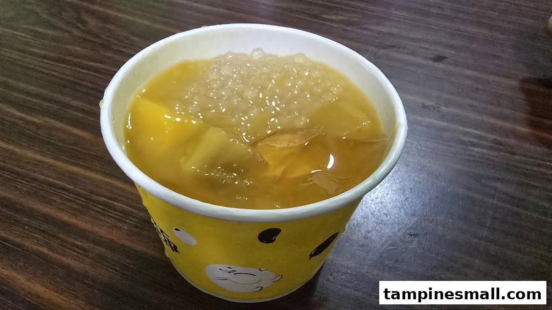 A vibrant yellow drink with ice and toppings in a branded cup on a wooden surface.
