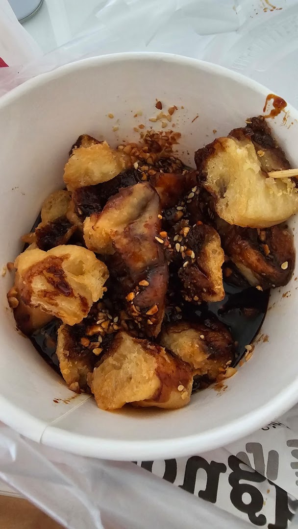 Fried dough fritters with sweet sauce and nuts in a white takeaway bowl.