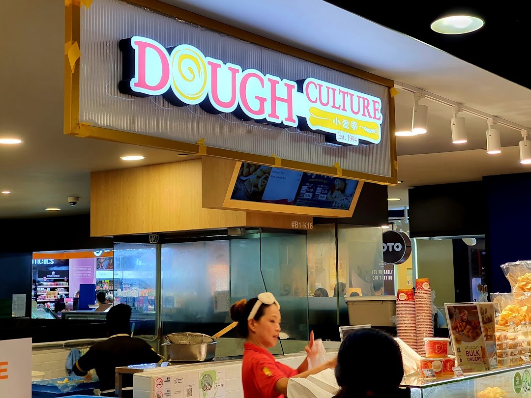The bustling counter of Dough Culture, featuring staff, fresh products, and the shop's illuminated sign.