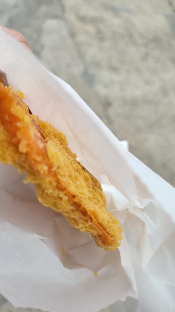 A close-up of a golden-brown fried dough fritter, partially wrapped in white paper.