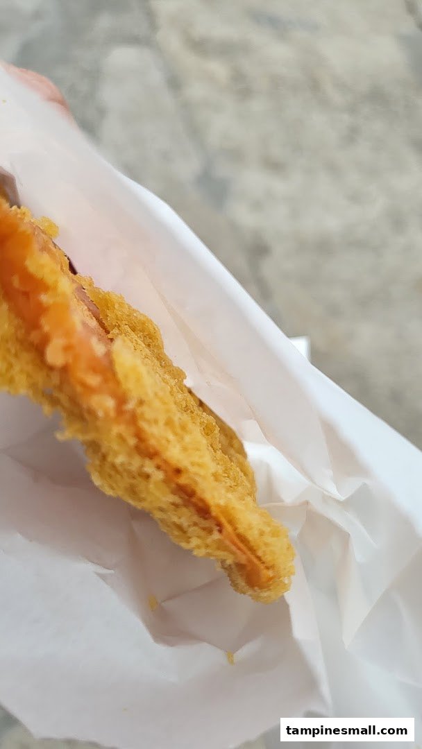 A close-up of a golden-brown fried dough fritter, partially wrapped in white paper.