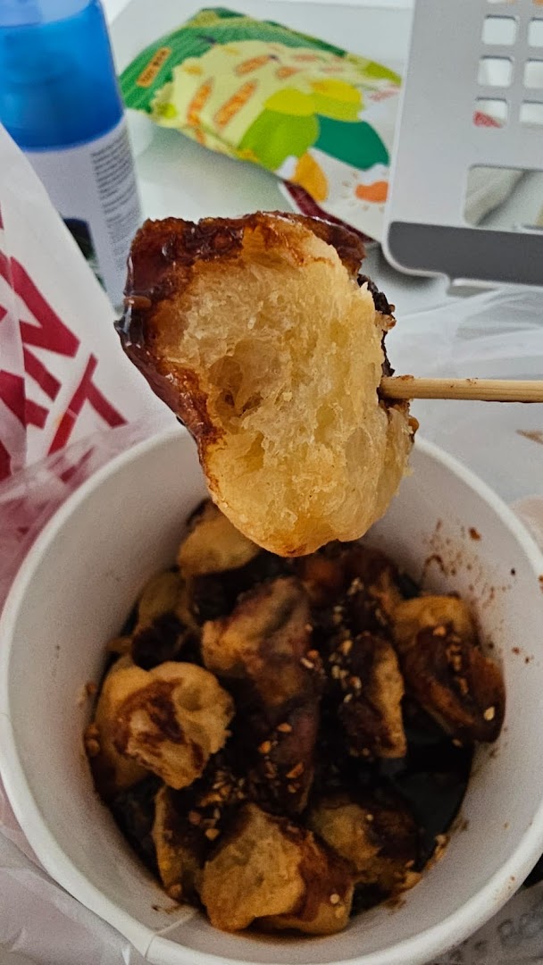 A close-up of a fried dough stick (youtiao) dipped in chocolate sauce with nuts, served in a cup.